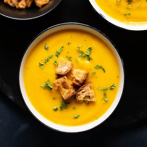 carrot soup in a cream bowl with croutons and chopped parsley on top