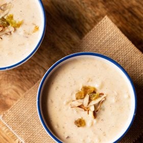 instant pot rice pudding in a blue rimmed white bowl garnished with raisins and almonds on a brown jute cloth.