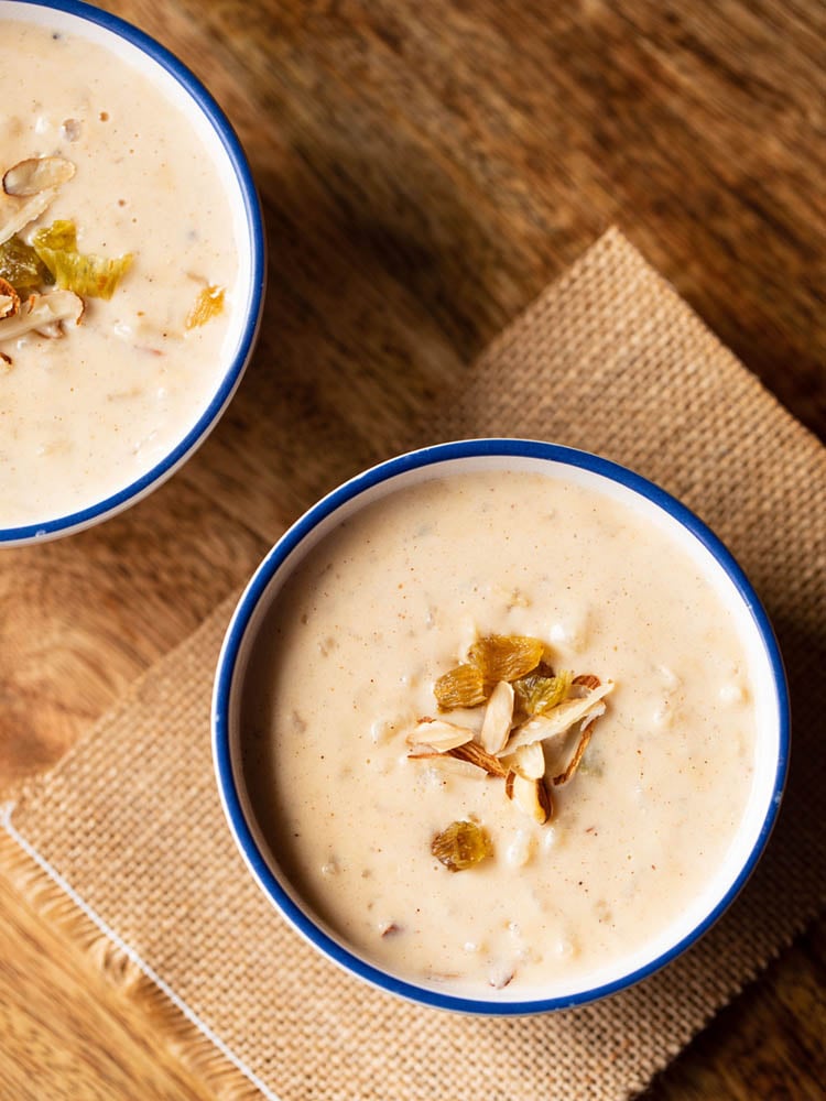 instant pot rice pudding in a blue rimmed white bowl garnished with raisins and almonds on a brown jute cloth.