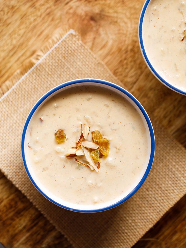 instant pot rice pudding in a blue rimmed white bowl garnished with raisins and almonds on a brown jute cloth.