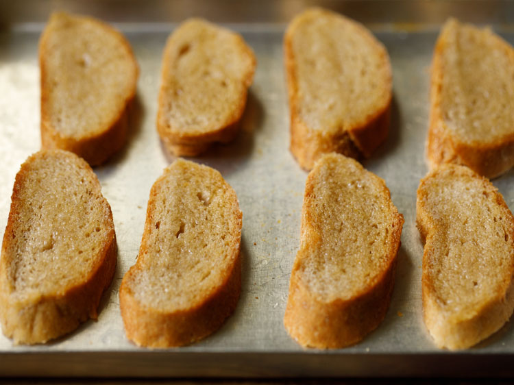 baguette slices brushed with olive oil and placed on baking tray to make croutons for french onion soup.