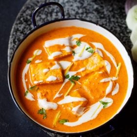 Paneer-Butter-Masala serviert in einer weißen Pfanne mit blauem Rand, garniert mit Sahne und Koriander