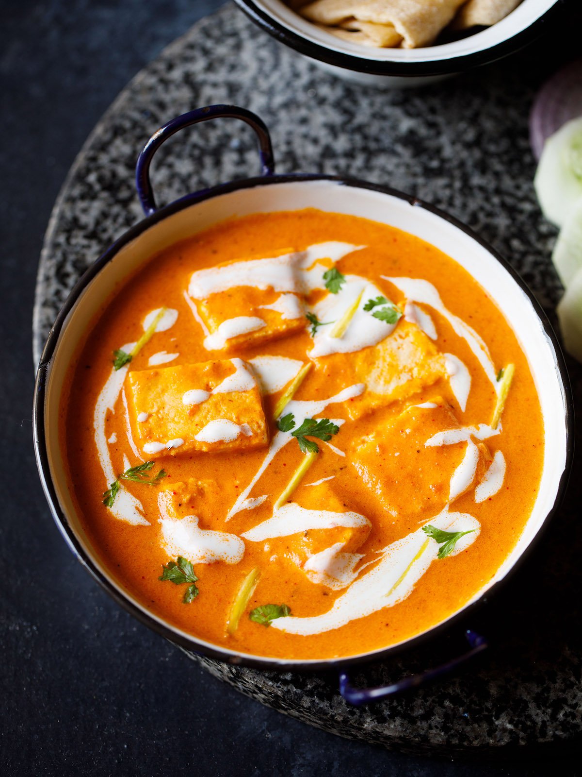 paneer butter masala served in a blue rimmed white pan, garnished with cream and cilantro