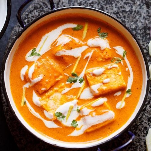paneer butter masala served in a blue rimmed white pan, garnished with cream and cilantro