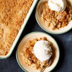apple crumble topped with a scoop of vanilla icecream in a green rimmed cream plate with a dessert spoon