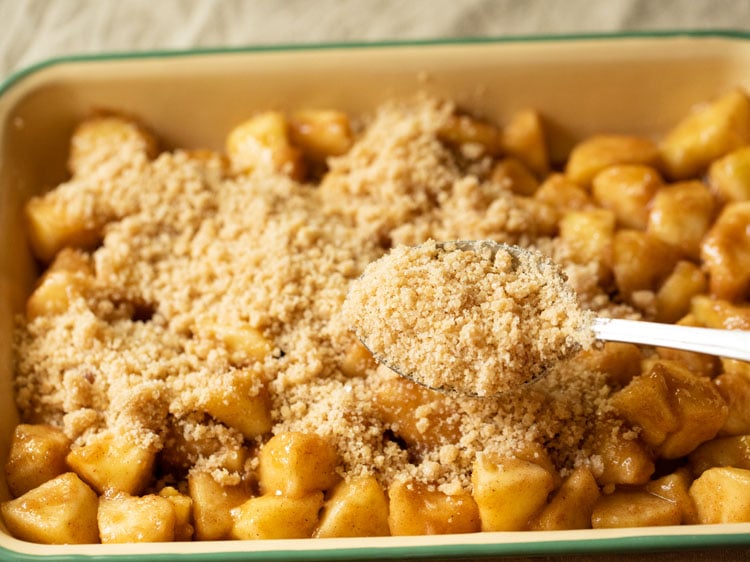 sprinkling streusel crumble topping  on the layered apples with a spoon