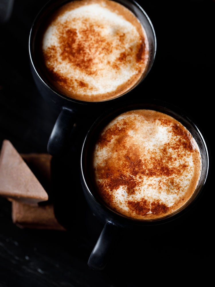 hot chocolate sprinkled with cocoa powder and served in 2 black cups on a black marble board