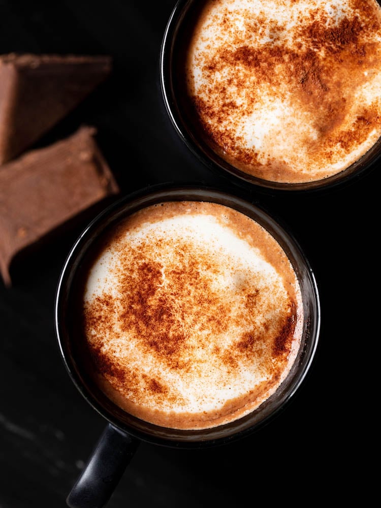 hot chocolate sprinkled with cocoa powder and served in 2 black cups on a black marble board