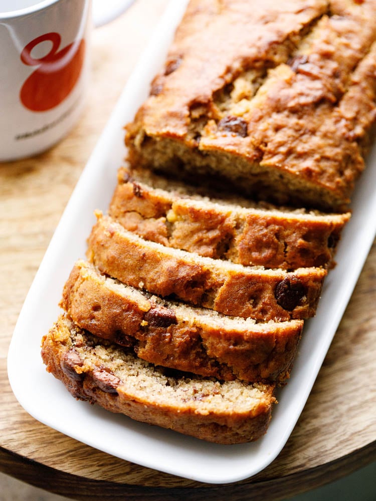 Chocolate Chip Banana Bread Loaf sliced on a white platter placed on a wooden board.