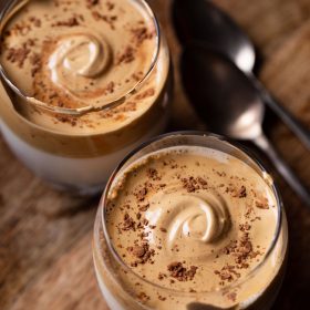 whipped coffee topped with some cocoa powder and served in two glasses on a brown wooden board