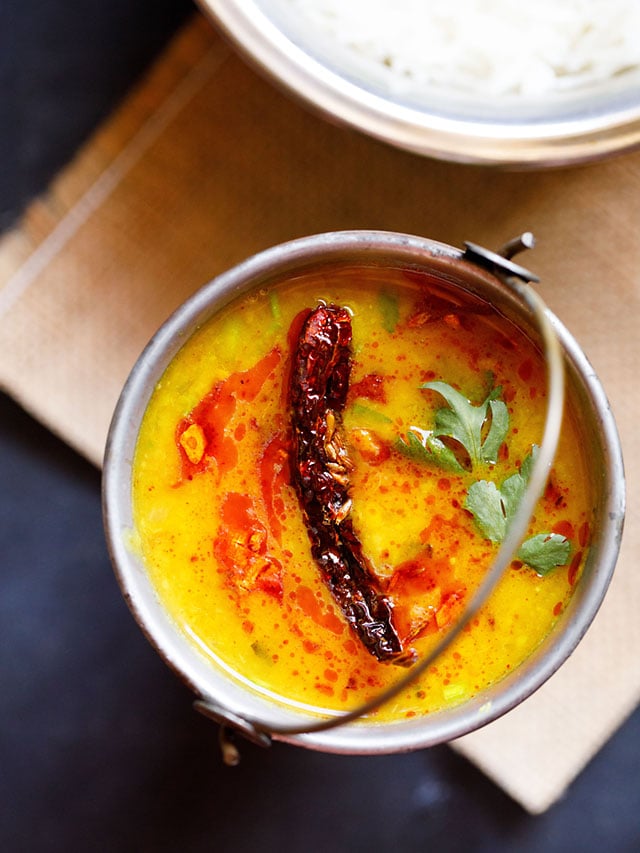 dal tadka garnished with cilantro and a topped with fried red chilli with some fried cumin and some red colored oil in a small brass bucket on a light brown jute mat