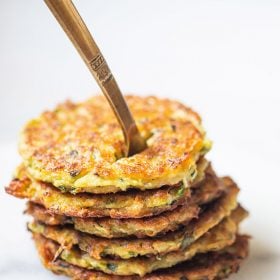 zucchini fritters stacked on top of each other with a brass fork inside them placed on a white marble board