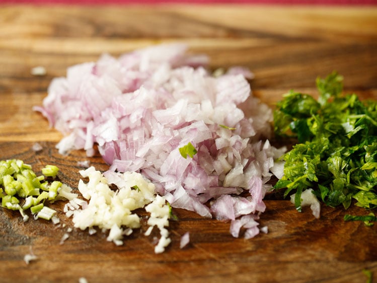 finely chopped onions, garlic, parsley and celery on a chopping board.