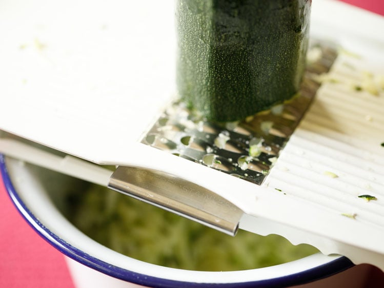 zucchini being grated on top of a bowl.