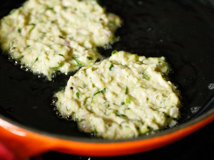 three zucchini fritter being fried in a skillet.