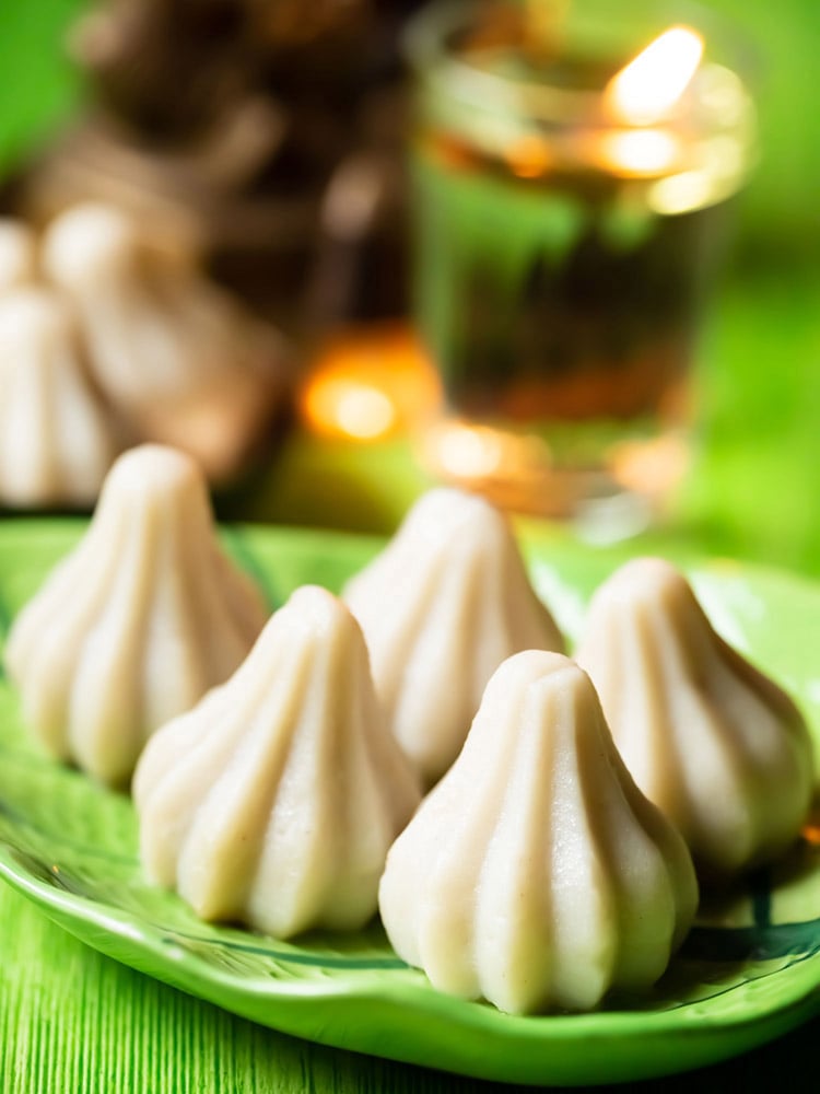 modak or modakam placed on a green leaf shaped platter on green colored board.