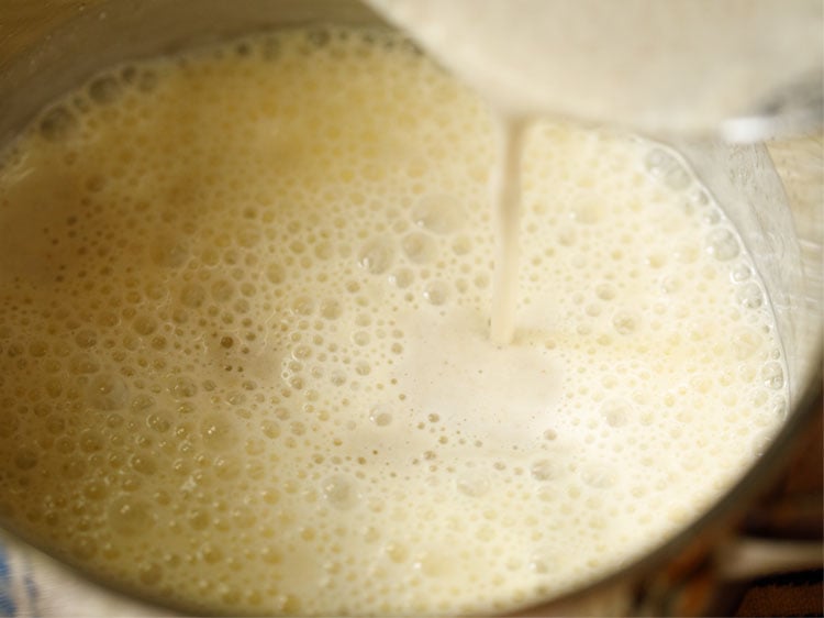 coconut paste being poured into buttermilk in a saucepan