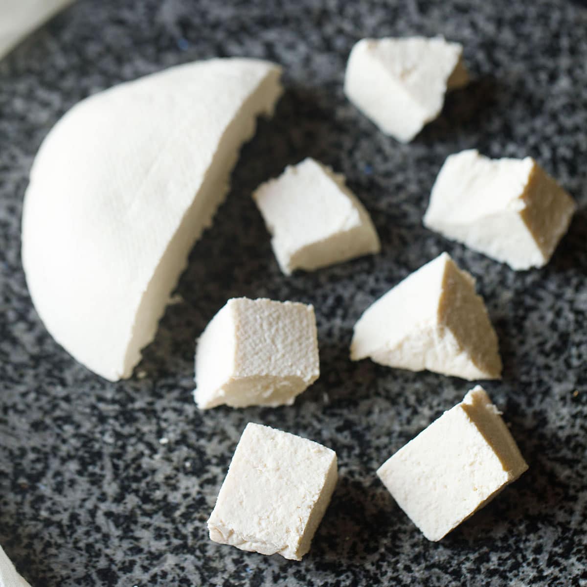 paneer cubes with a halved block of paneer on a black granite board