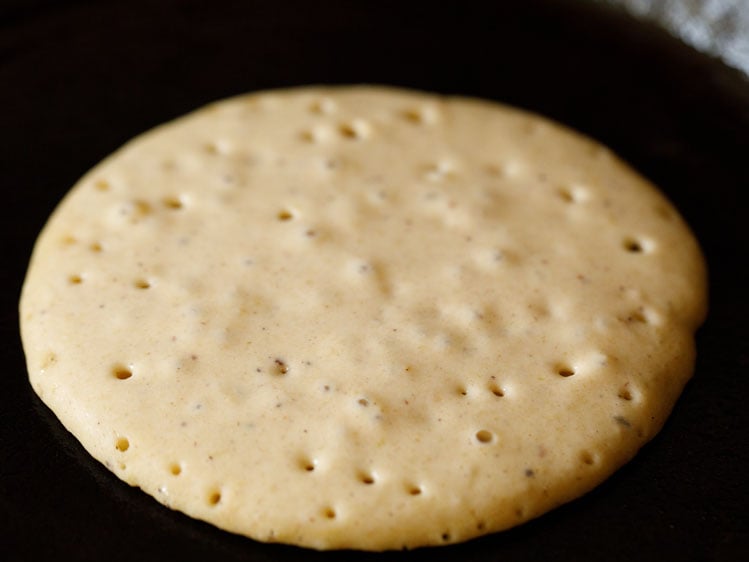 pumpkin pancake cooking on skillet has bubbles starting to form.