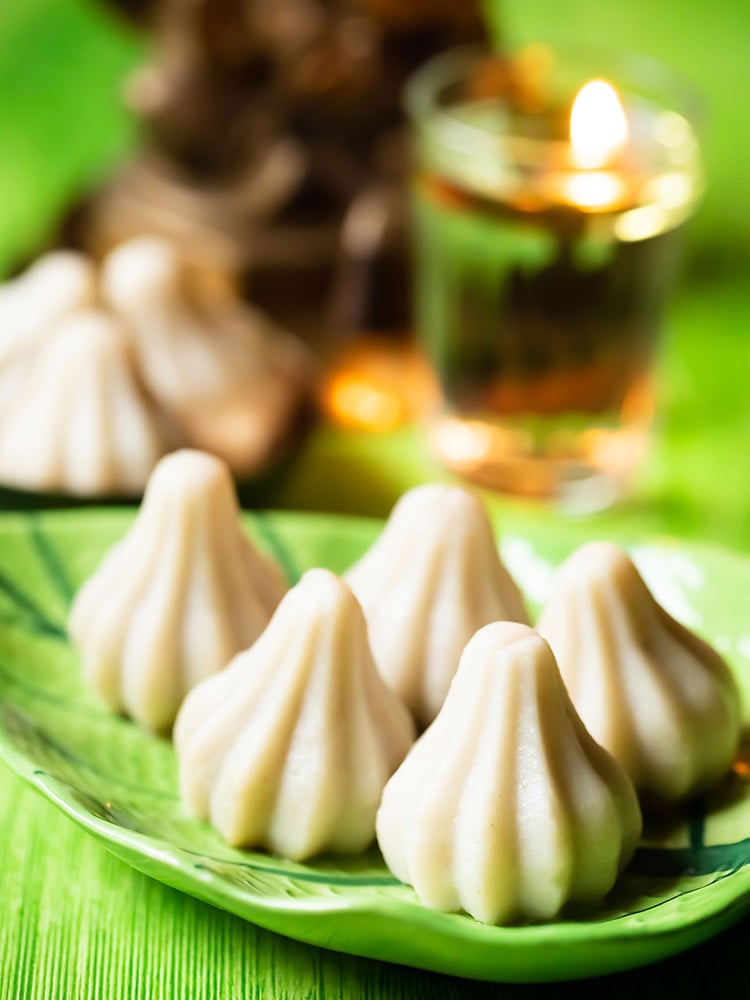 ukadiche modak placed on a green leaf shaped platter on a green colored board