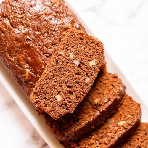 chocolate zucchini bread partly sliced with one slice kept on top of the loaf on a white rectangular tray on a white marble background