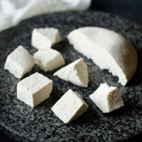 paneer block halved and cut in cubes on a grey-black granite round board