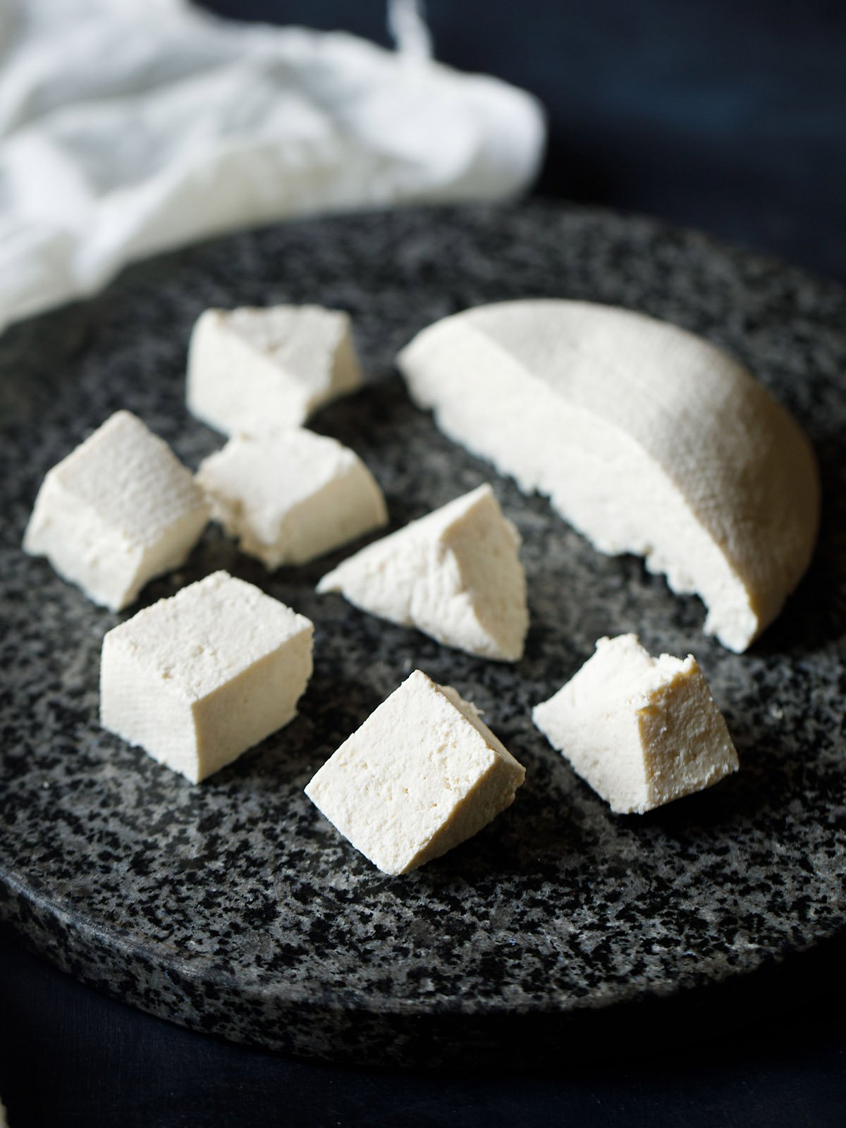 paneer block halved and cut in cubes on a grey-black granite round board