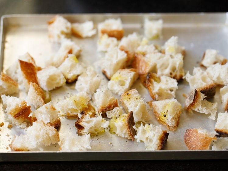 cubed bread drizzled with olive oil and crushed black pepper in a metal baking tray