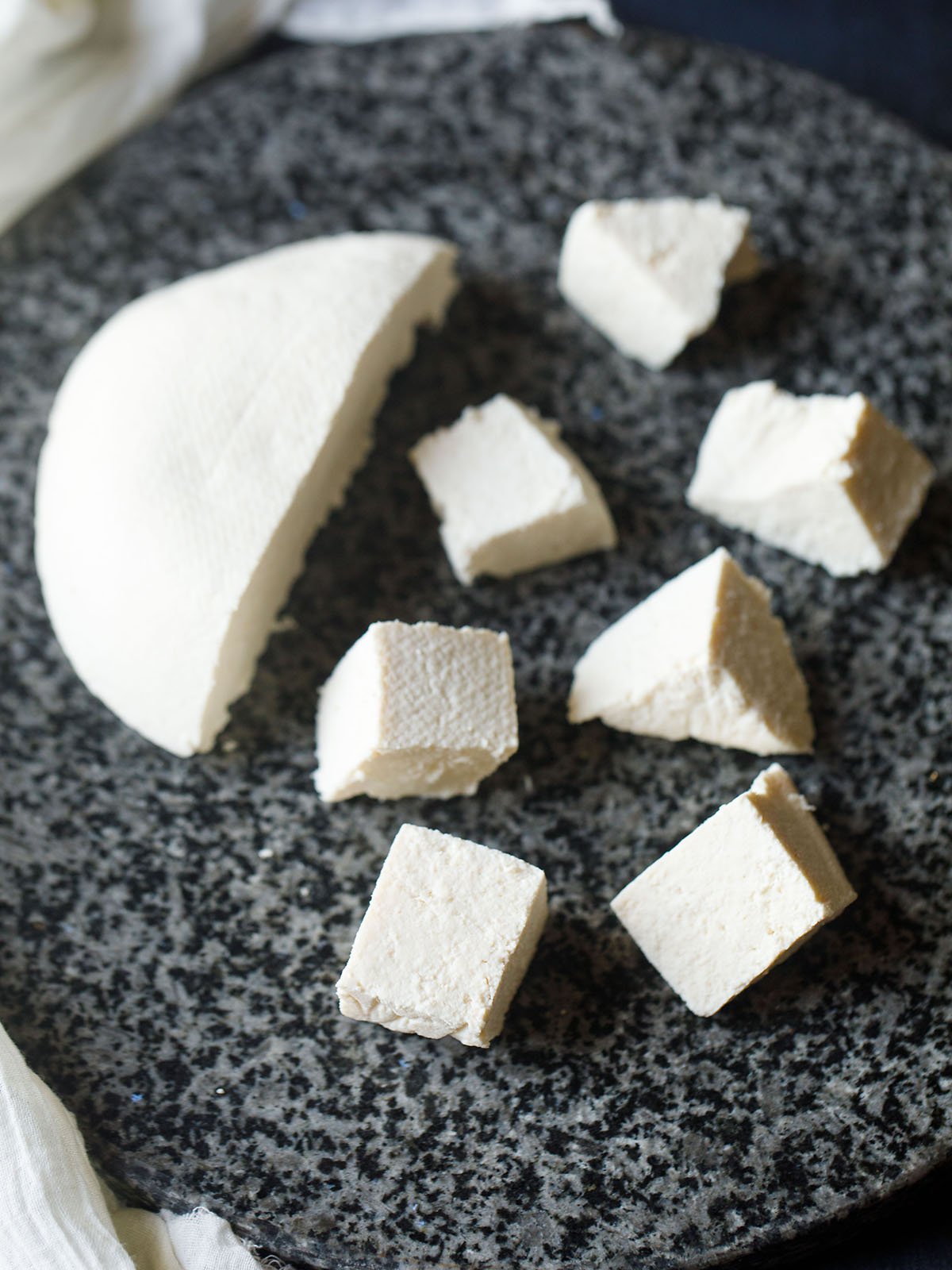 paneer cheese halved and cut in cubes on a grey-black granite round board