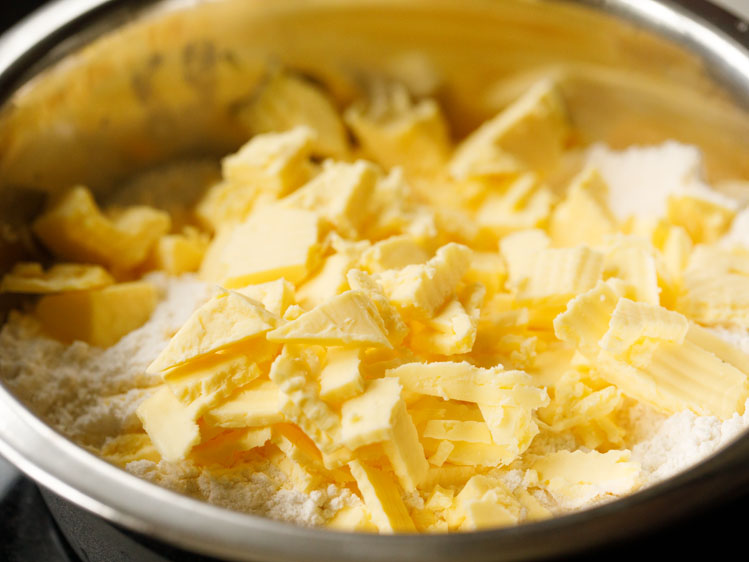 small cubes of butter added to the top of the flour mix in a silver mixing bowl