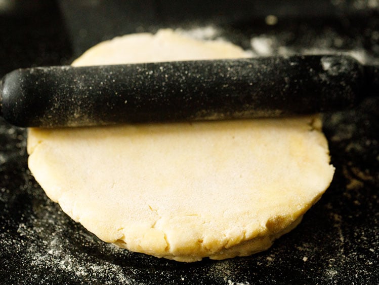 black rolling pin rolling out pie crust on a black surface
