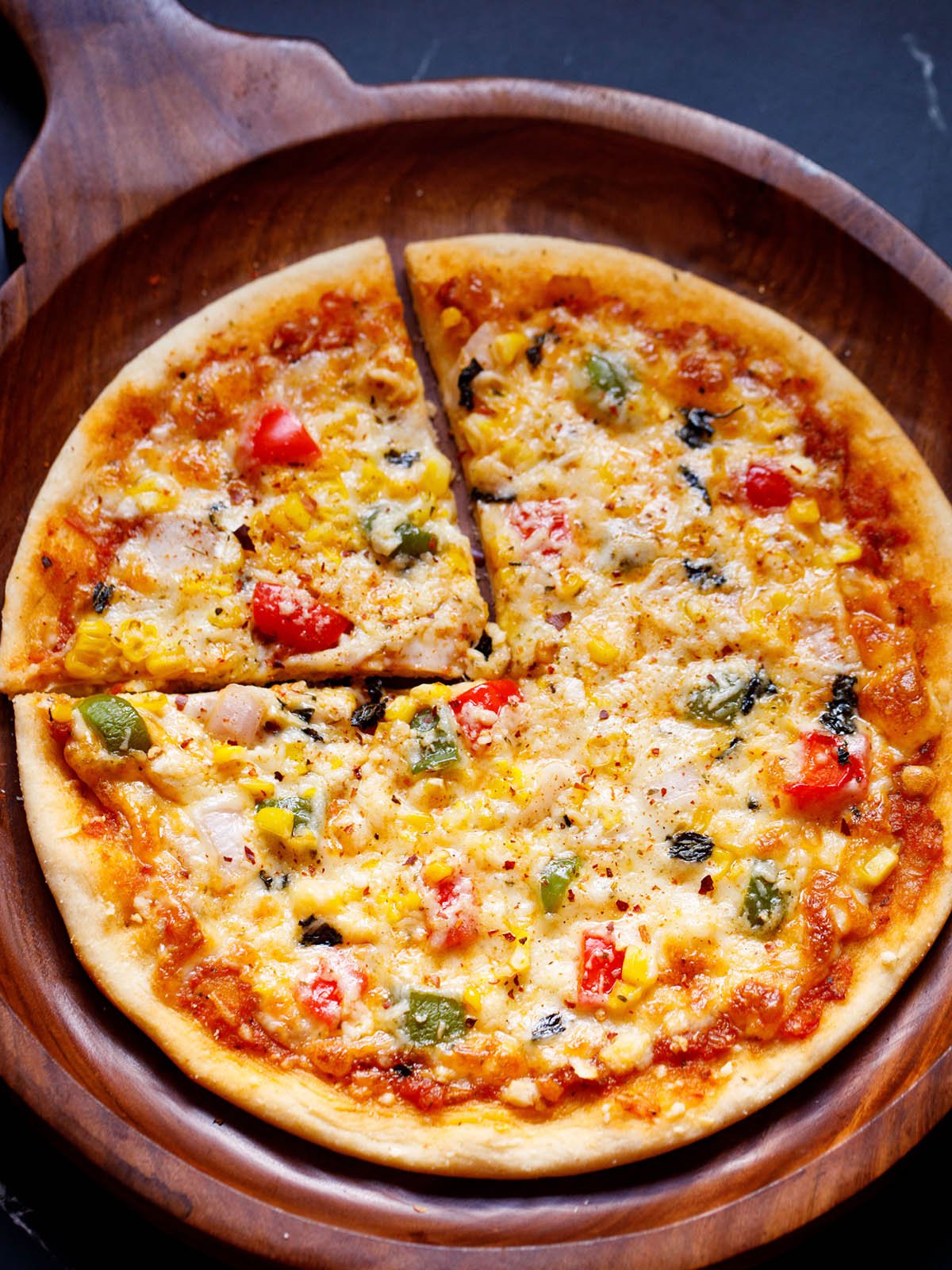 Whole round Pizza on a wooden pizza plate with a cut triangular slice on left top side