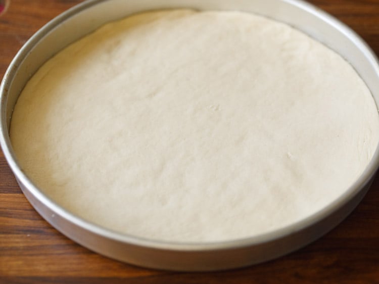 pizza crust placed in the greased baking tin