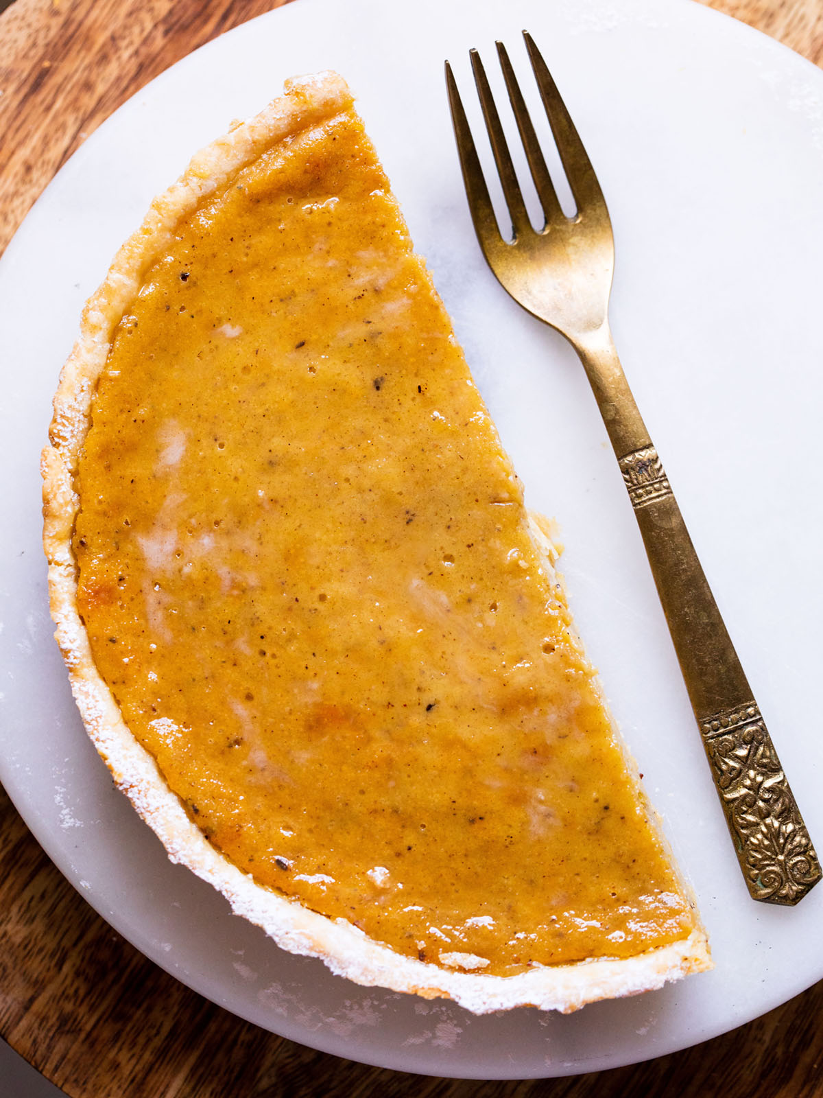 half of an eggless pumpkin pie in an all butter homemade pie crust on a white serving platter with a brass fork