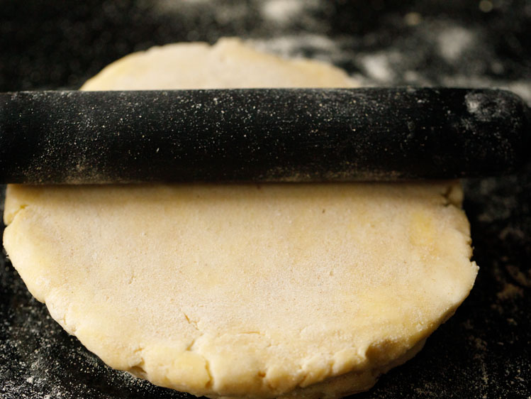 black rolling pin rolling out a round of homemade pie dough on a lightly floured black surface
