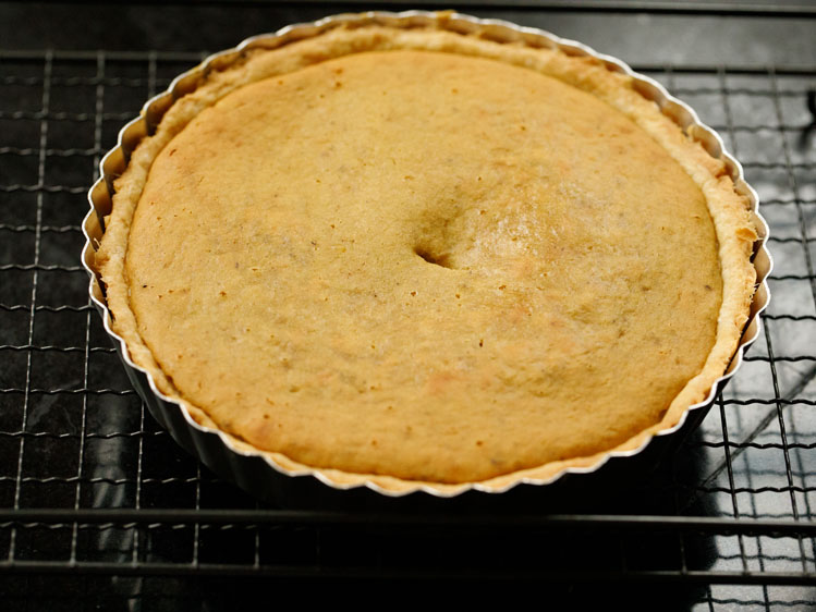 baked eggless pumpkin pie in a silver pie tin on a cooling rack