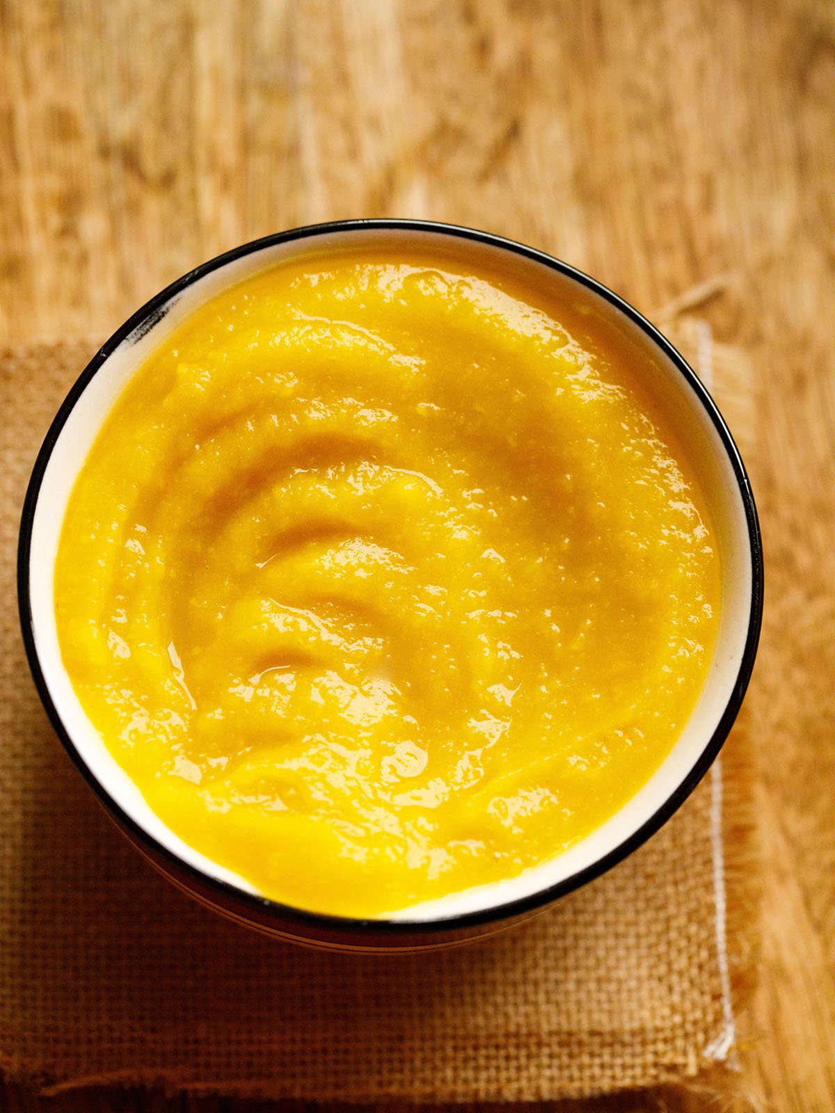 homemade pumpkin purée in a white bowl with a black rim on a light brown jute fabric