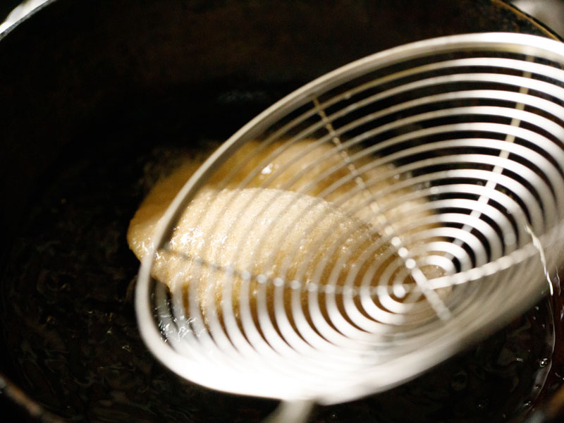 metal spider spoon being used to nudge the puri so that it puffs completely