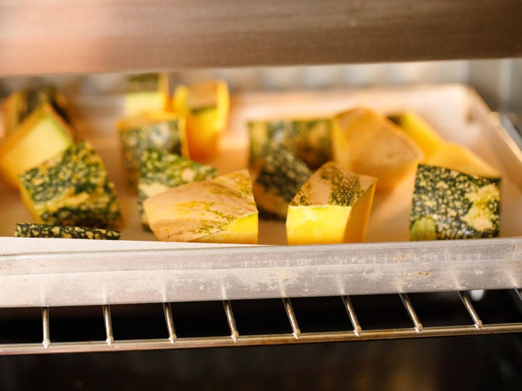 cubed kabocha squash on a parchment lined baking sheet in the oven