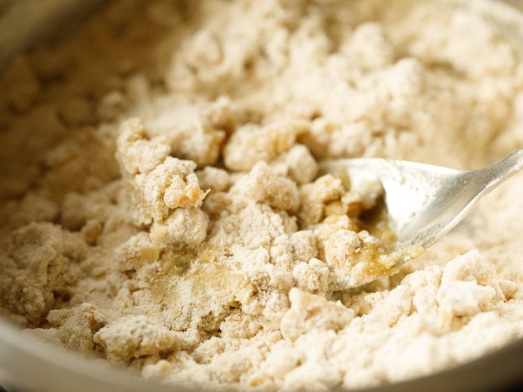 dry flour mixture after mixing with ghee in a silver mixing bowl with a silver spoon