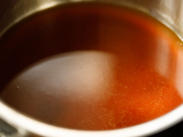 jaggery melted in water in a dark, caramel colored simple syrup in a silver saucepan