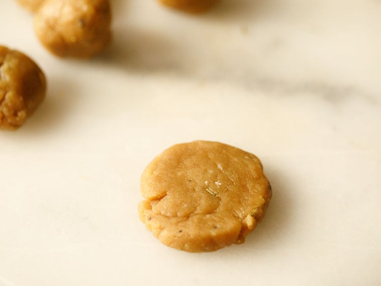 thekua dough balls on a white surface, with one that has been flattened