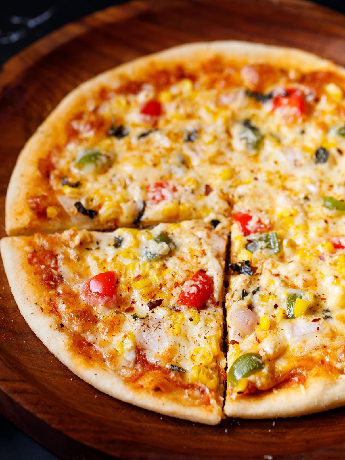 veg-pizza a triangular slice of veg pizza with the remaining pizza on a wooden pizza plate sprinkled with some dried herbs and red chilli flakes