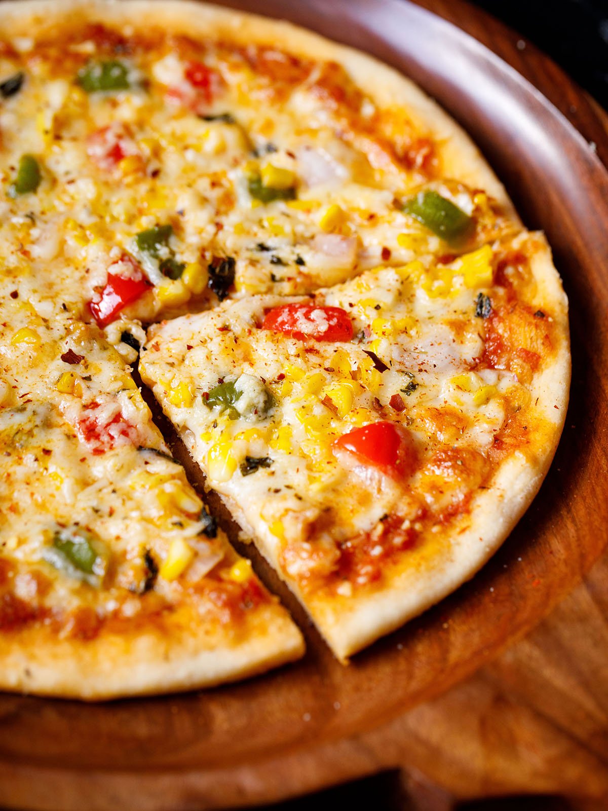 sliced pizza with the remaining pizza on a wooden pizza plate sprinkled with some dried herbs and red chilli flakes