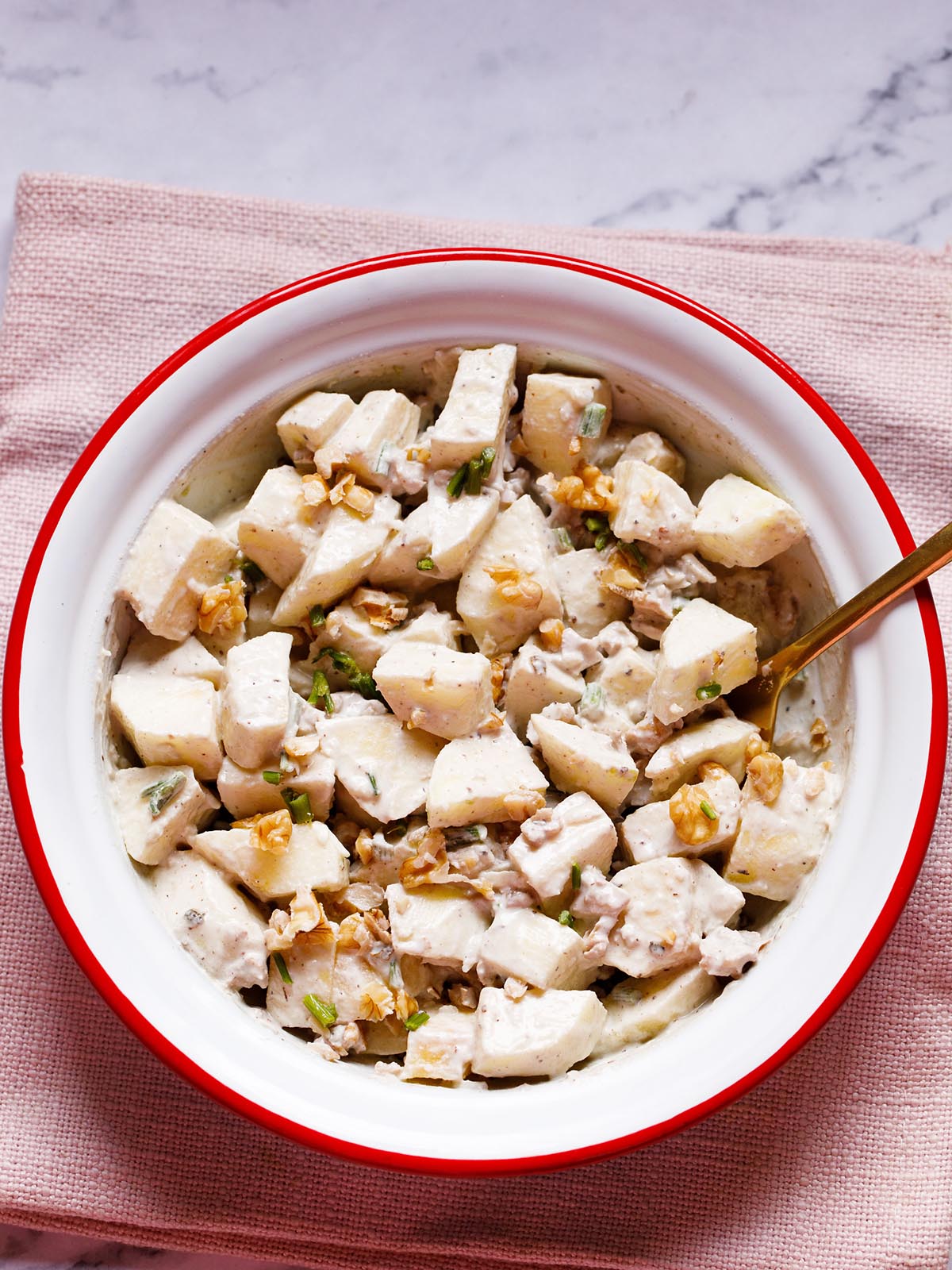 easy, creamy apple salad in a white and red ceramic bowl with a brass spoon a white background