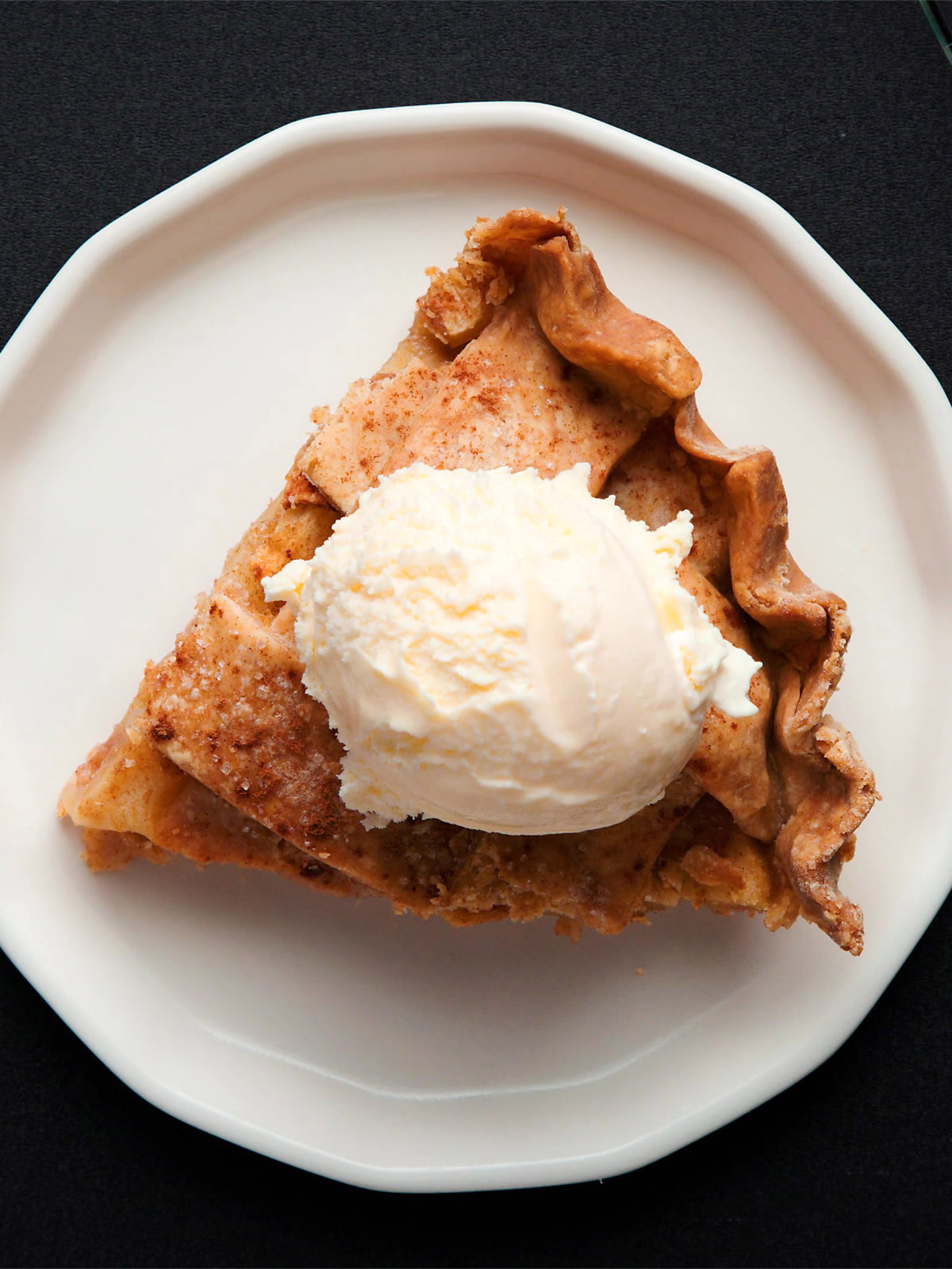 an apple pie wedge slice topped with vanilla ice cream on an off-white plate