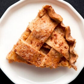 a triangular wedge of apple pie on an off-white plate
