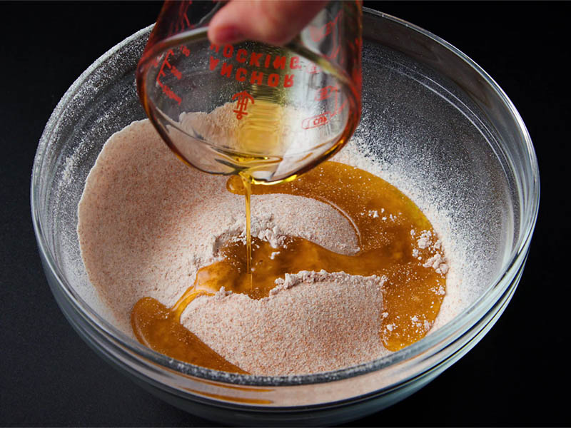 olive oil being added to the sifted ingredients in a glass bowl