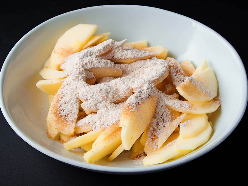 brown sugar and wheat flour added on sliced apples in a white bowl