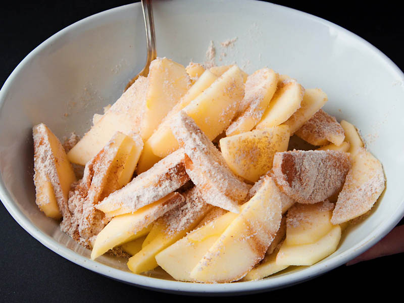 flour and sugar being mixed with apples with a spoon